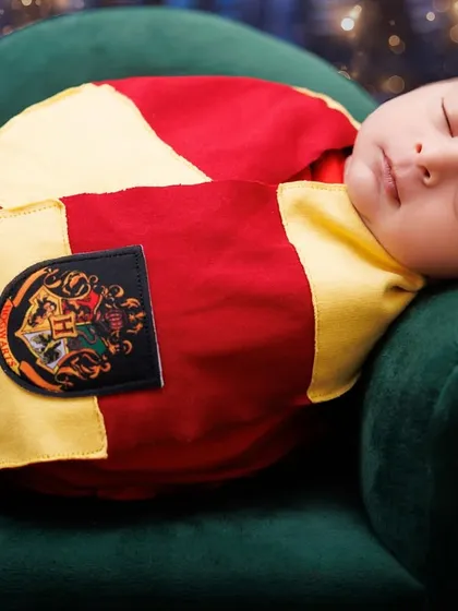 A sleeping newborn dressed as Harry Potter, resting on a green armchair. A close-up shot capturing their peaceful expression.