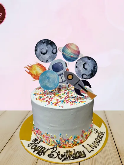 A galaxy-themed cake topped with planets, an astronaut, and a rocket ship. The colorful sprinkles around the base add a touch of starry fun.