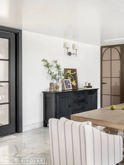 A black sideboard provides a strong visual anchor and practical storage. The mix of modern and traditional elements, like the French doors and contemporary wall sconces, creates a balanced design.