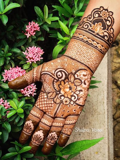 A beautiful floral design on the palm, set against a background of pink flowers, showing the inspiration behind the art.