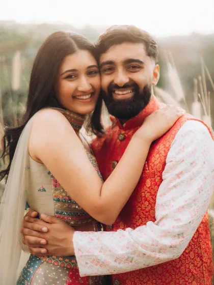 A bright and happy portrait of Rahul and Anjali hugging in a field of tall grass. Their joyful expressions are what make this photo so special.