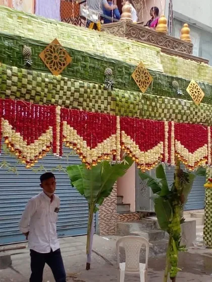 A close-up of a traditional 'Chappra' decoration for a home event. This temporary roof structure is made of woven palm leaves and adorned with beautiful garlands of red and white flowers.