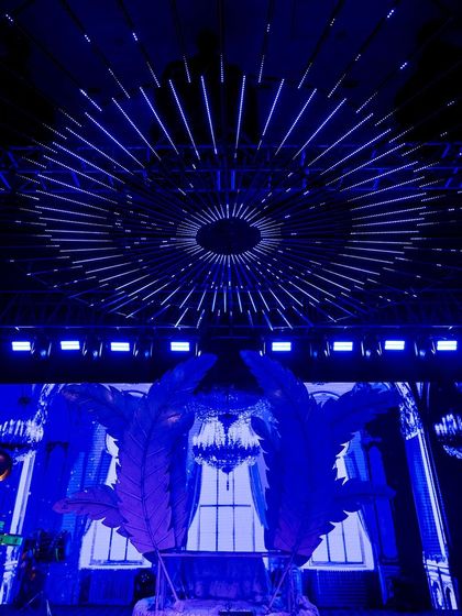 A futuristic Sangeet stage with a massive LED screen backdrop and large, feather-like set pieces, creating a dynamic and visually stunning setting for performances.