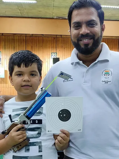 A proud moment for a young participant and his coach. After learning the basics of aiming and firing, he holds up his first target sheet, showing the tangible results of his focus and our expert guidance.