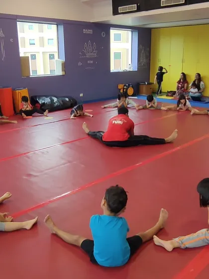 Children practice their straddle stretches together, learning about flexibility and following their coach's lead in a group setting.