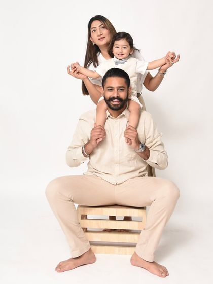 A fun and playful family pose for a first birthday shoot. The toddler sits on dad's shoulders, creating a dynamic and joyful image against a minimalist white backdrop.