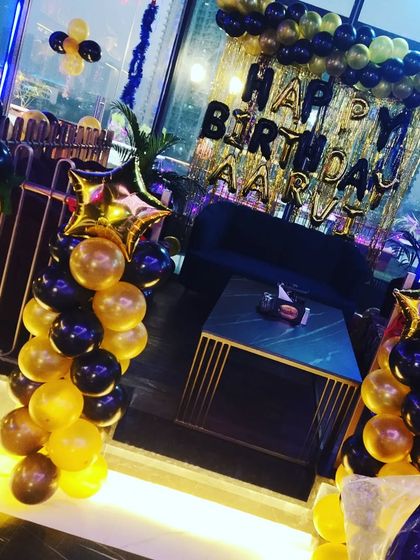 A birthday setup in a high-rise restaurant, with black and gold balloons framing the view.