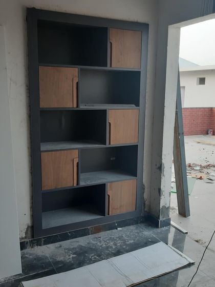 A custom shelving unit for an office reception being assembled. The two-tone design with wood-finish shutters and a dark grey frame is visible even during the construction phase.