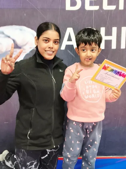 A happy toddler and her coach celebrate a new certificate with matching peace signs.