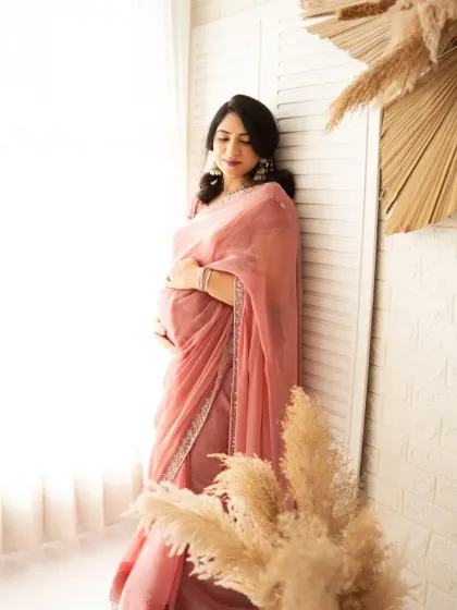 A serene solo portrait of an expecting mother in a beautiful pink saree. The soft window light and gentle pose create a timeless and graceful image.