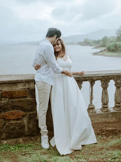 A full-length portrait of a couple in coordinated white outfits, sharing a quiet moment by the water. This showcases a classic, timeless pre-wedding photography style.