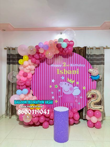 A playful Peppa Pig theme for Ishani's 2nd birthday. The setup includes a striped pink backdrop with Peppa, a colorful balloon arch, and a themed cake stand.