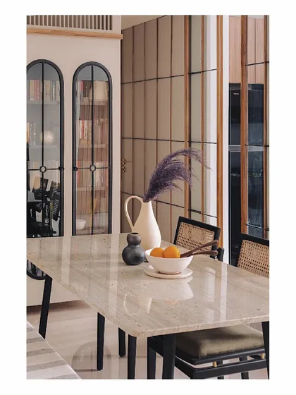 A view across the marble dining table, showing the arched bookshelves in the background. The composition of clean lines, natural materials, and curated objects creates a space that is soothing, comfortable, and very elegant.