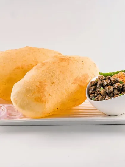 Fluffy Chole Bhature ready to be eaten. The high-key lighting and white background make the image pop, focusing all attention on the perfectly puffed bhature and the accompanying spicy chole.