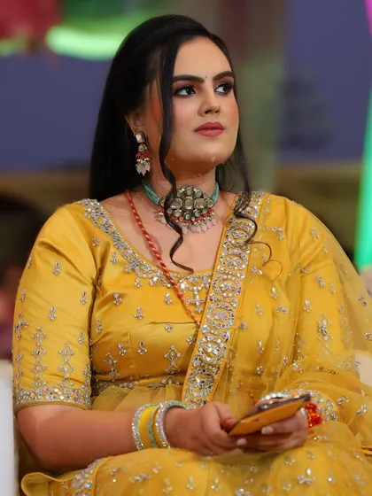 A candid moment from a Sangeet night. Her makeup, featuring a soft smokey eye and a neutral lip, was designed to look beautiful under the colorful event lighting.