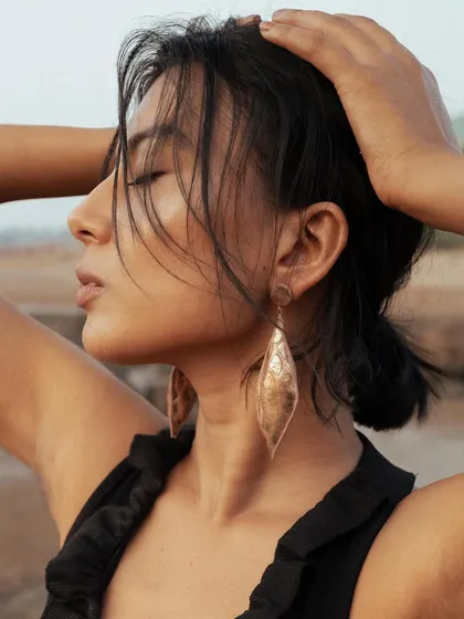 A profile shot from the jewelry campaign, highlighting the textured, messy updo. The look is designed to feel natural and windswept, as if styled by the sea breeze.