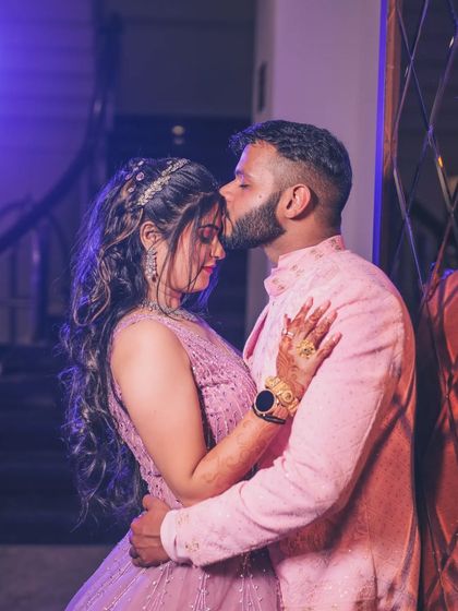 A tender moment between a couple, as the groom kisses the bride's forehead under a soft purple light.