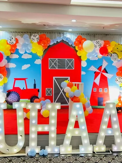 We design fun and colorful farm-themed parties that kids adore. This complete stage setup includes a bright red barn backdrop, a tractor cutout, a windmill, and large marquee letters spelling out the birthday boy's name, perfect for a second birthday bash.