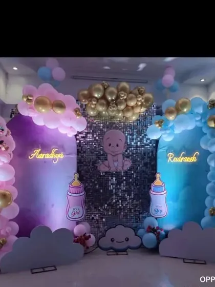 A dual-themed baby shower for twins or a gender reveal. The backdrop is split into pink and blue sections with matching balloon arches and neon signs for each name.