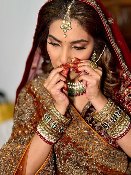 A classic bridal pose, adjusting the nose ring. This candid shot captures the traditional details of the look.
