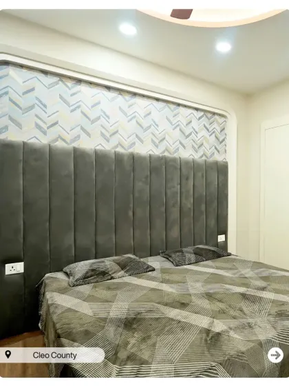 This bedroom features a tall, channel-tufted grey headboard set against a chevron-patterned wallpaper, creating a sophisticated and modern look.