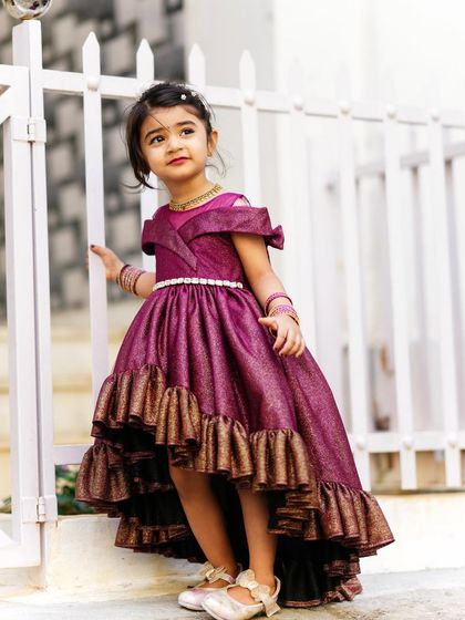 A little girl looking like a princess in her ruffled purple gown, posing by a white fence for her third birthday pictures.