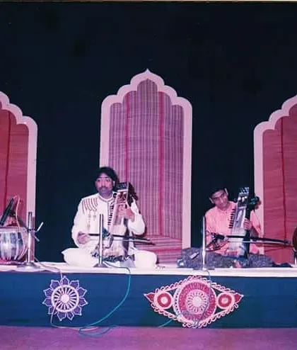 A photograph from an older concert, performing with a full Indian classical ensemble. I am providing the rhythmic foundation for sarangi, esraj, and tanpura players on a traditionally decorated stage.