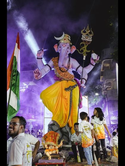 A full-length view of the Kopri Cha Samrat idol at night, with the Indian flag visible, capturing a moment of patriotic and religious fervor.