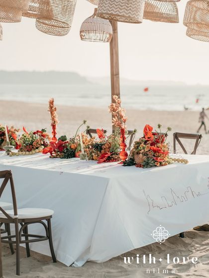A long table at the beach event, with a custom-illustrated runner and hanging rattan lamps.