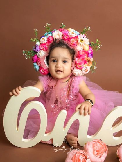 A beautiful portrait of the one-year-old girl holding a "One" sign, surrounded by pink flowers.