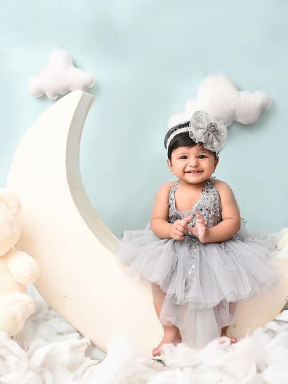 A happy smile from this little girl on her moon and clouds set. The silver-grey dress and teddy bear complement the dreamy blue backdrop perfectly.