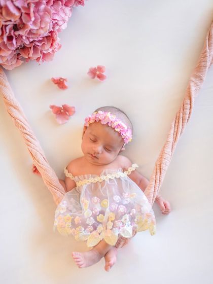Another angle of the newborn on the floral swing, this time with pink petals scattered around her, adding to the dreamy feel.