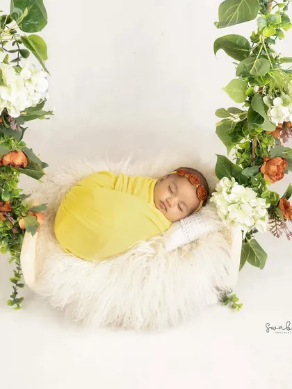 A beautiful swing decorated with lush flowers and greenery holds a peacefully sleeping baby. This setup creates a whimsical and enchanting portrait.