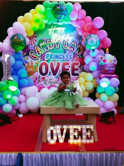 A colorful "Candy Land" themed first birthday, with the birthday girl sitting on a stage filled with sweet-treat props and rainbow balloons.
