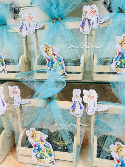 A close-up of the adorable Peter Rabbit themed hampers. The wooden crates are wrapped in blue tulle and decorated with character cutouts, making them a charming gift for a baby announcement.