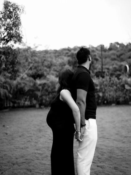 A black and white shot of the couple standing back-to-back while holding hands, looking out in opposite directions. It's an artistic pose symbolizing their unity and individual strength.