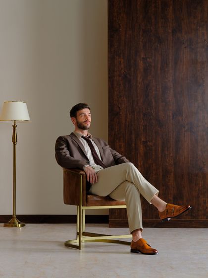 Another look from the same commercial shoot, this time featuring a relaxed, seated pose. The styling with a brown blazer and tan trousers creates a warm, approachable, and aspirational image.
