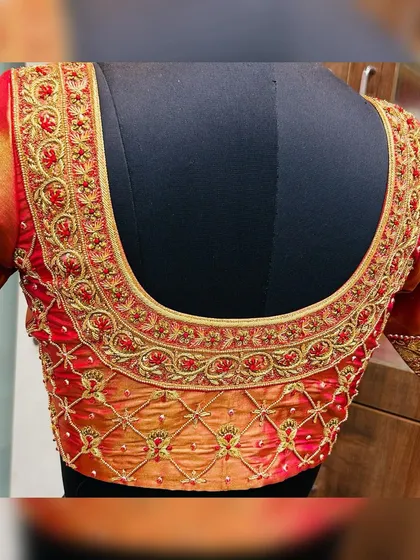 For the classic bride, this dual-tone red and orange silk blouse is a timeless choice. The U-shaped back is adorned with traditional floral vine aari work in gold thread, creating an opulent look that perfectly complements a wedding saree.