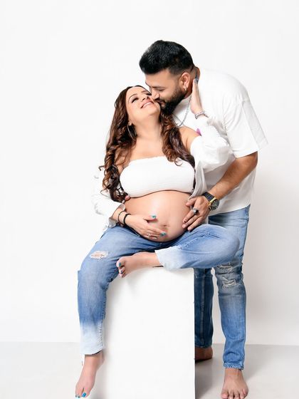 A happy and intimate moment from a casual jeans-and-tee session. The focus is on their joyful expressions and the excitement of expecting.