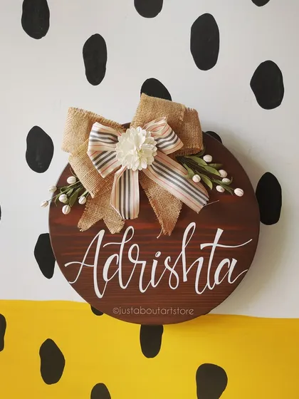 A straight-on shot of the "Adrishta" name board, showcasing the beautiful burlap bow with its handmade flower and delicate details.