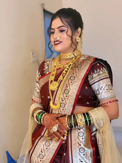 A full view of the bride's maroon saree look. The green and gold bangles provide a beautiful contrast against the deep red of her saree.