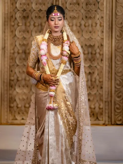 A bride stands in her white and gold Kanjivaram saree, complete with a sheer, embellished veil. This look is perfect for a serene and elegant wedding ceremony.