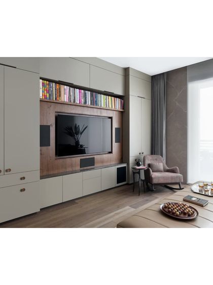 The media wall in the family lounge is designed to be both functional and aesthetically pleasing. Custom cabinetry in a soft grey finish conceals storage, while a wood-paneled niche frames the television and integrated speakers, keeping the look clean and uncluttered.