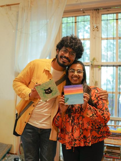 A couple proudly displays their finished artwork after a fun and creative "Paint with Kittens" session.