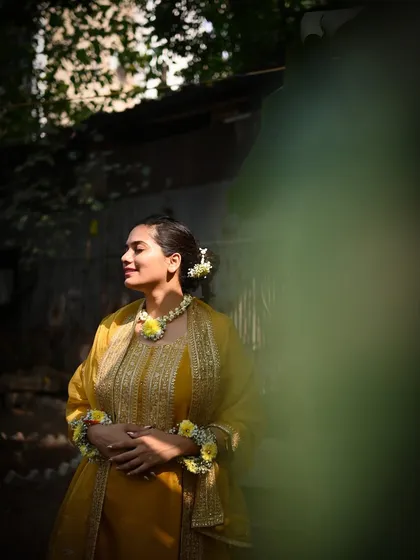 A bride basking in the sun during her Haldi ceremony. The beautiful side lighting highlights her floral jewelry and the peaceful, happy glow on her face.