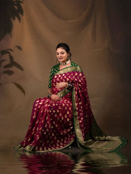 A traditional and graceful maternity portrait. The client is seated, wearing a beautiful magenta and green saree, creating a culturally rich and elegant image against a classic painted backdrop.