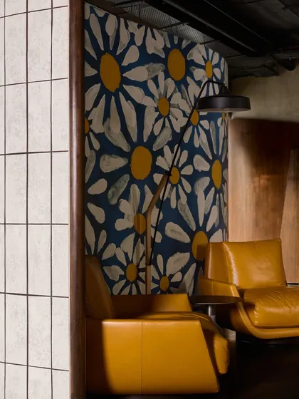 A close-up of the junction between a tiled column, the floral art screen, and the modern armchairs, showcasing a playful mix of patterns and textures.