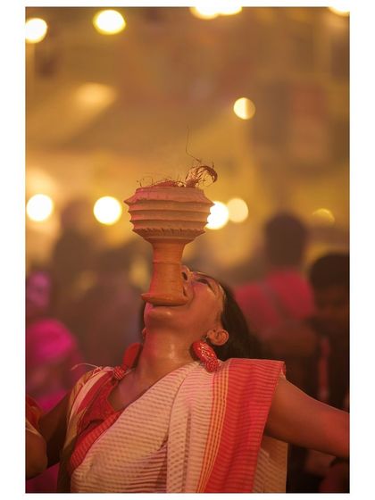 A woman dances with a dhunuchi, the bokeh of lights in the background adding to the magical atmosphere of the evening Aarti.