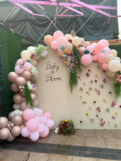 A 'Baby in Bloom' photo backdrop with a beautiful arch of pink and dusty rose balloons, accented with fresh flowers and greenery.