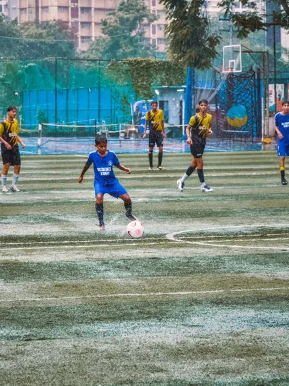 A young player from our U-12 team controls the ball with confidence, looking for a pass during a rainy match. This demonstrates the composure and field awareness we develop in our players.